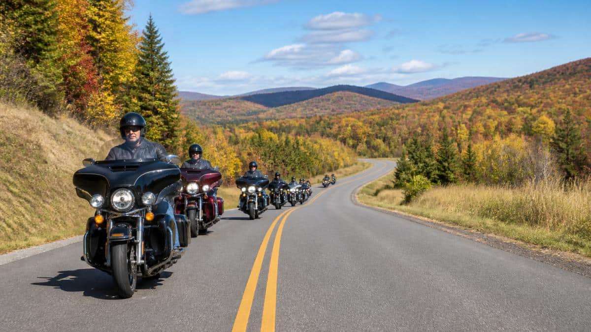 Group of motorcycle riders on a scenic rural highway with rolling hills, clear blue skies, and autumn foliage, riding in organized formation with helmets on