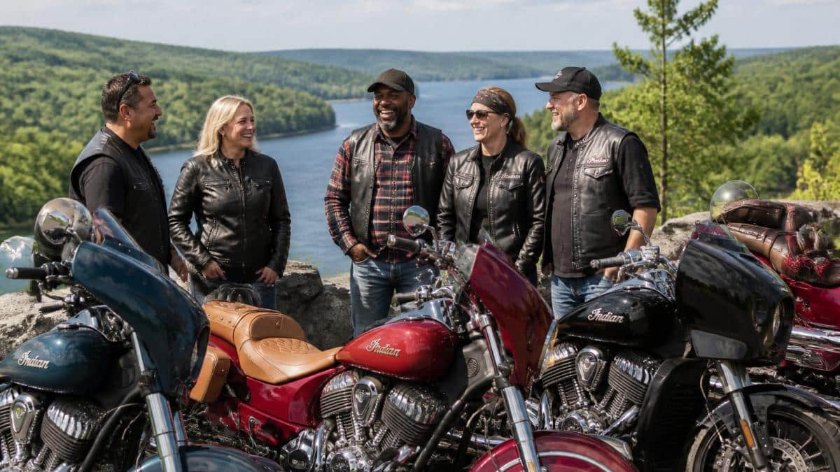 Diverse group of motorcycle riders standing together with their bikes at a scenic overlook, laughing and conversing, showing genuine camaraderie and connection